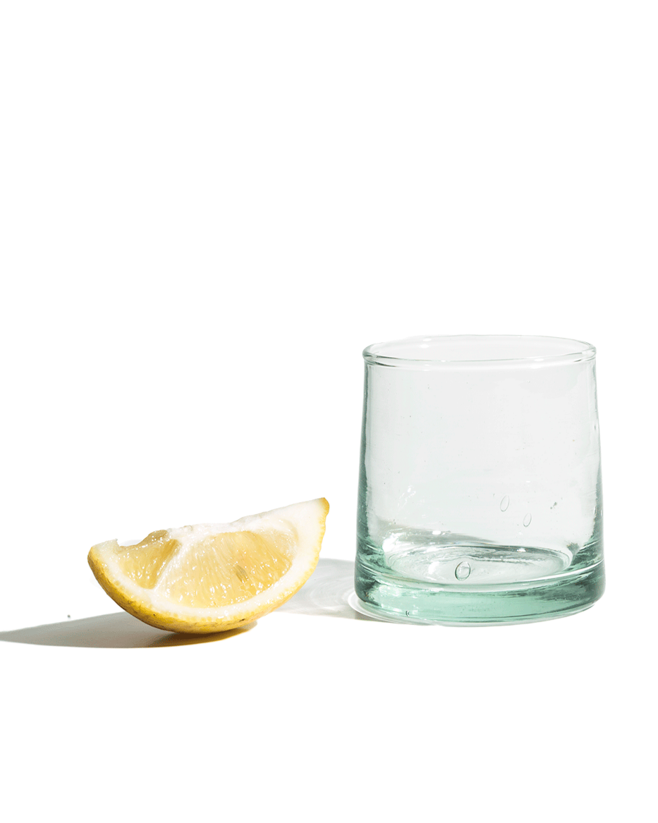 Clear glass tumbler next to a lemon wedge on a white background