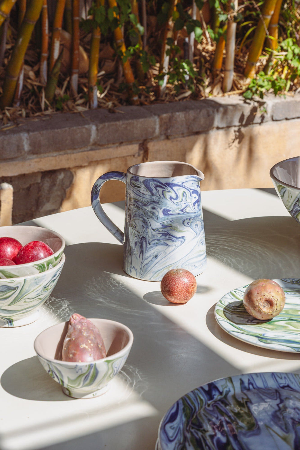 Decorative ceramic items including a pitcher, bowls, and plates on a table outdoors.