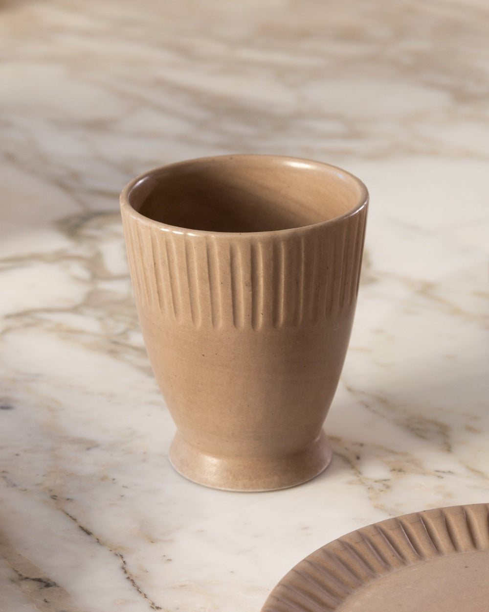Brown ceramic cup with ribbed texture on a marble surface