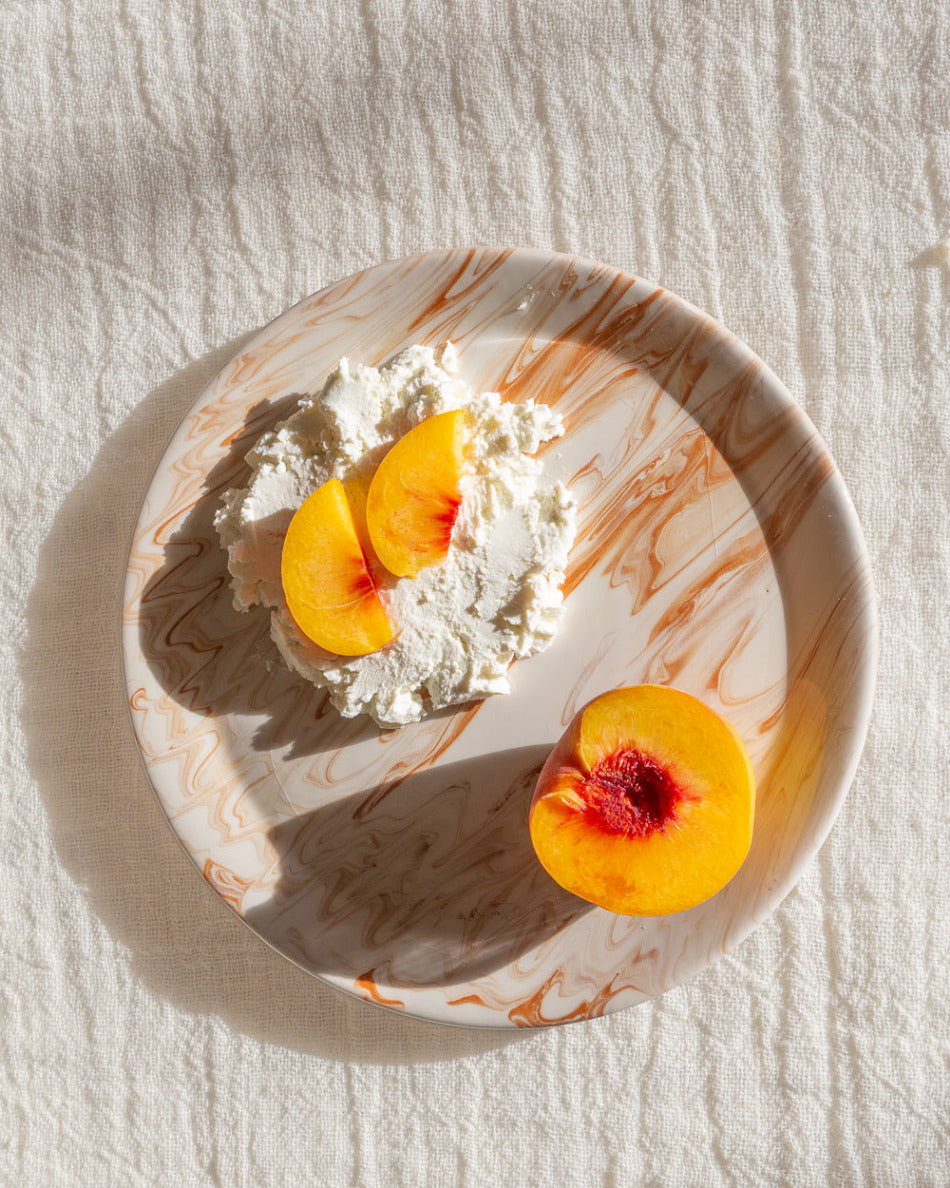 Marble-patterned plate with peaches and cream on a textured white surface