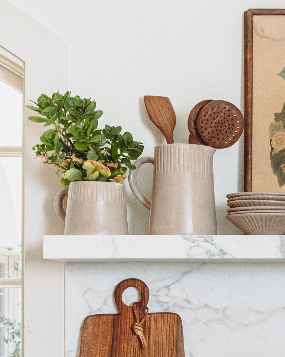 Kitchen shelf with ceramic pots, wooden utensils, and a plant on a marble countertop.