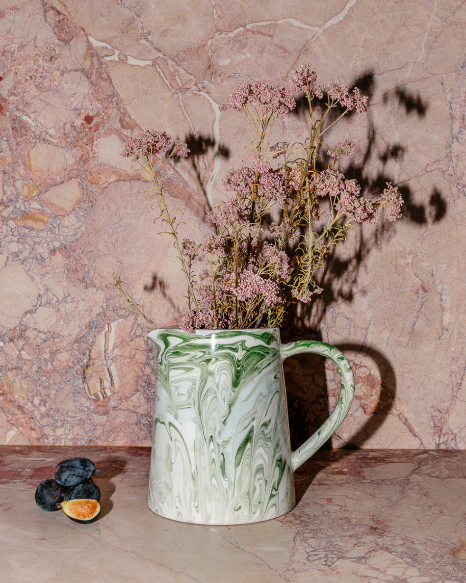 Green marbled pitcher with dried flowers against a marble wall.