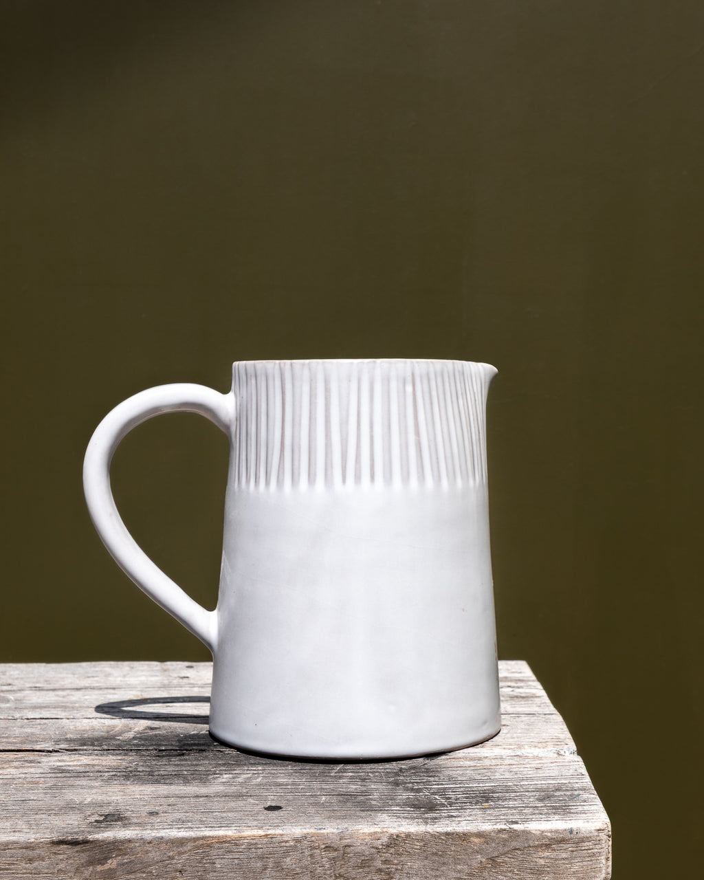 White ceramic pitcher with textured design on a wooden surface against a dark background