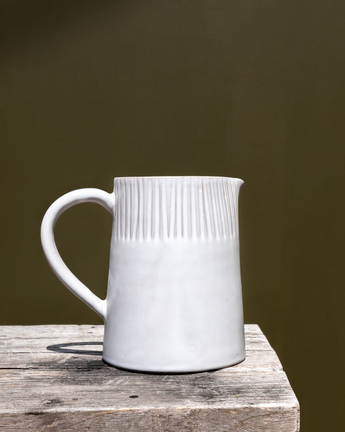 White ceramic pitcher with textured design on a wooden surface against a dark background