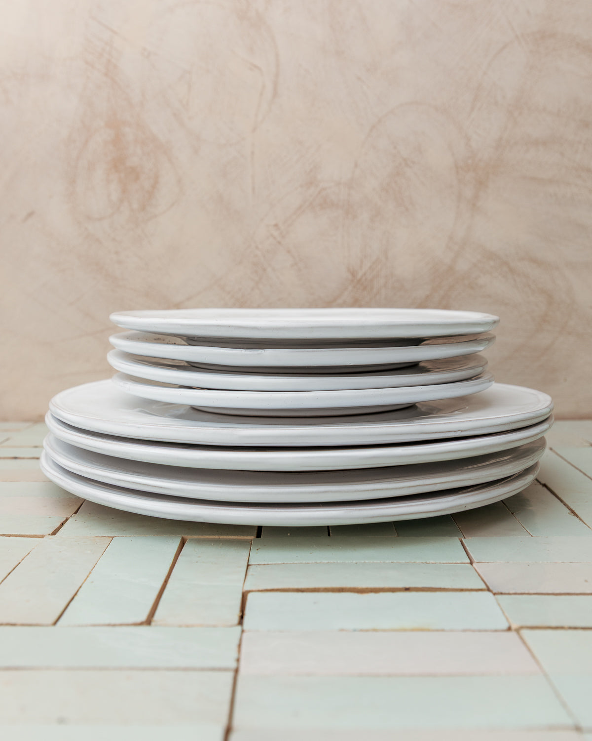 Stack of white ceramic plates on a tiled floor with a wooden wall background