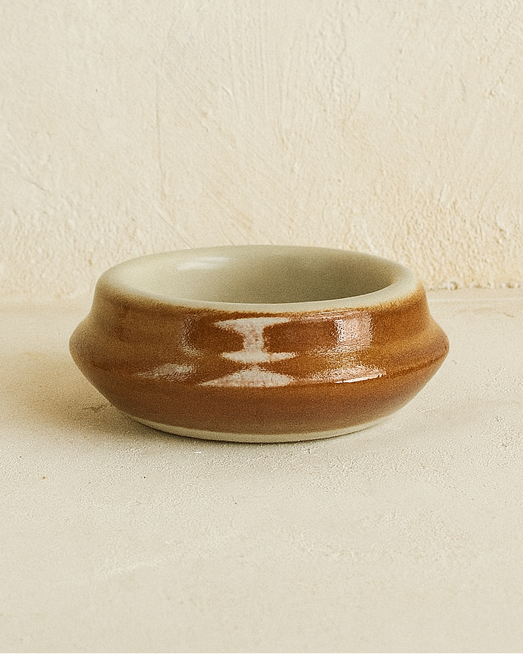 Ceramic butter bowl with brown exterior and white interior on a beige surface