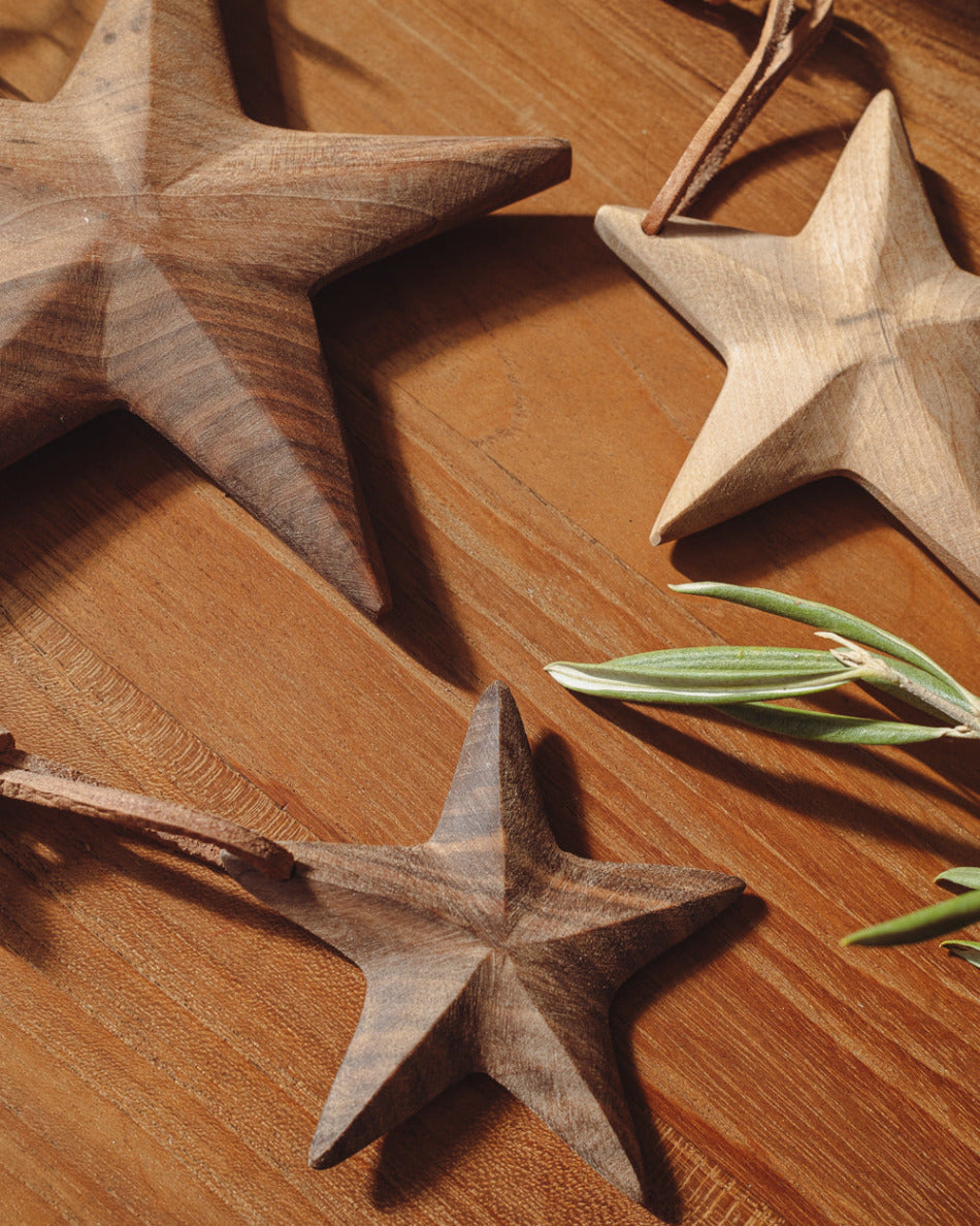 Three wooden star-shaped decorations on a wooden surface with a small green leaf.