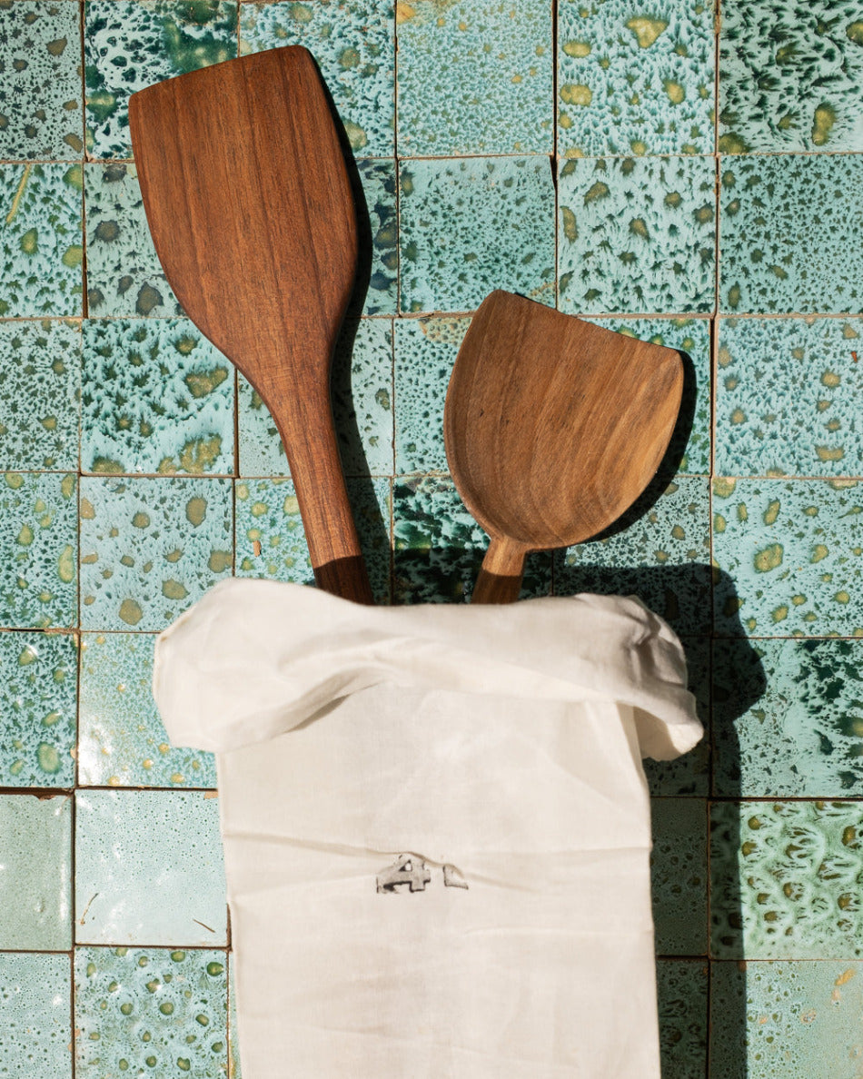 Wooden spatulas in a white bag against a green tiled wall
