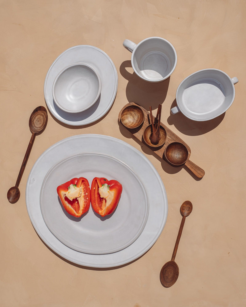 Table setting with white plates, cups, and red bell peppers on a beige background