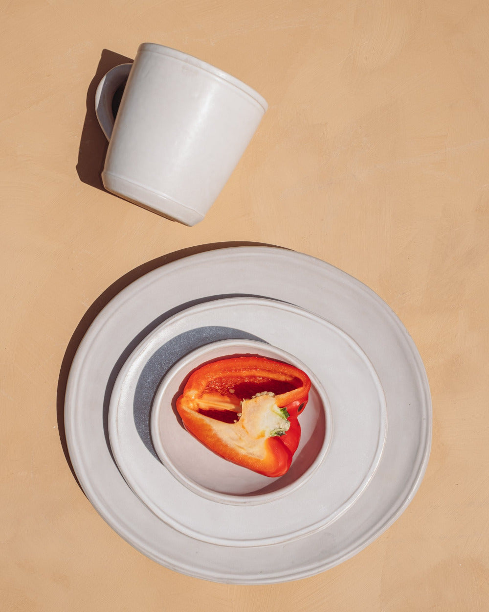 White mug and plate with a red pepper on a beige background