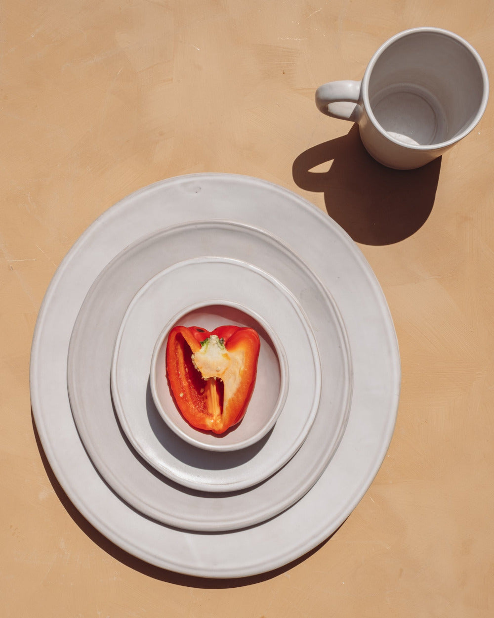 Red bell pepper on a white plate with a white mug on a beige surface