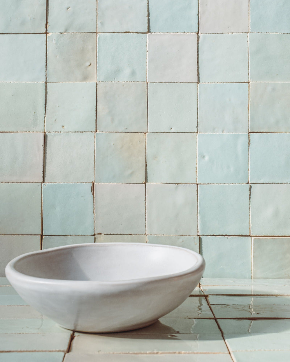 White oval bowl in front of a water green zellige tile background