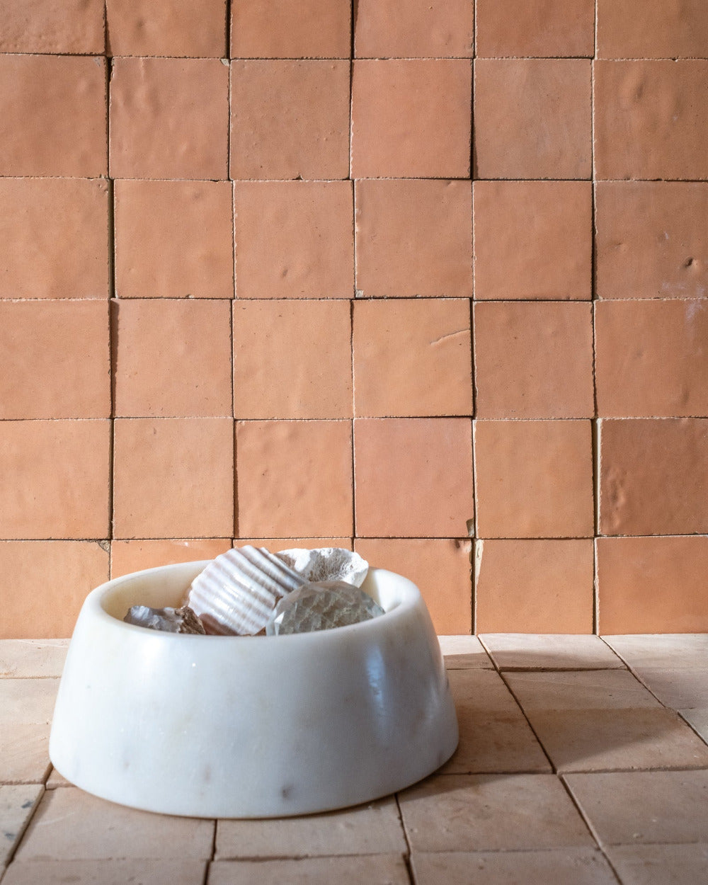 White marbled bowl with tseashells  on a zellige tiled floor against a coral zelige tiled wall.