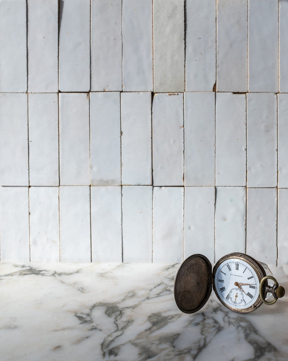 Vintage pocket watch on a marble surface with a tiled wall background