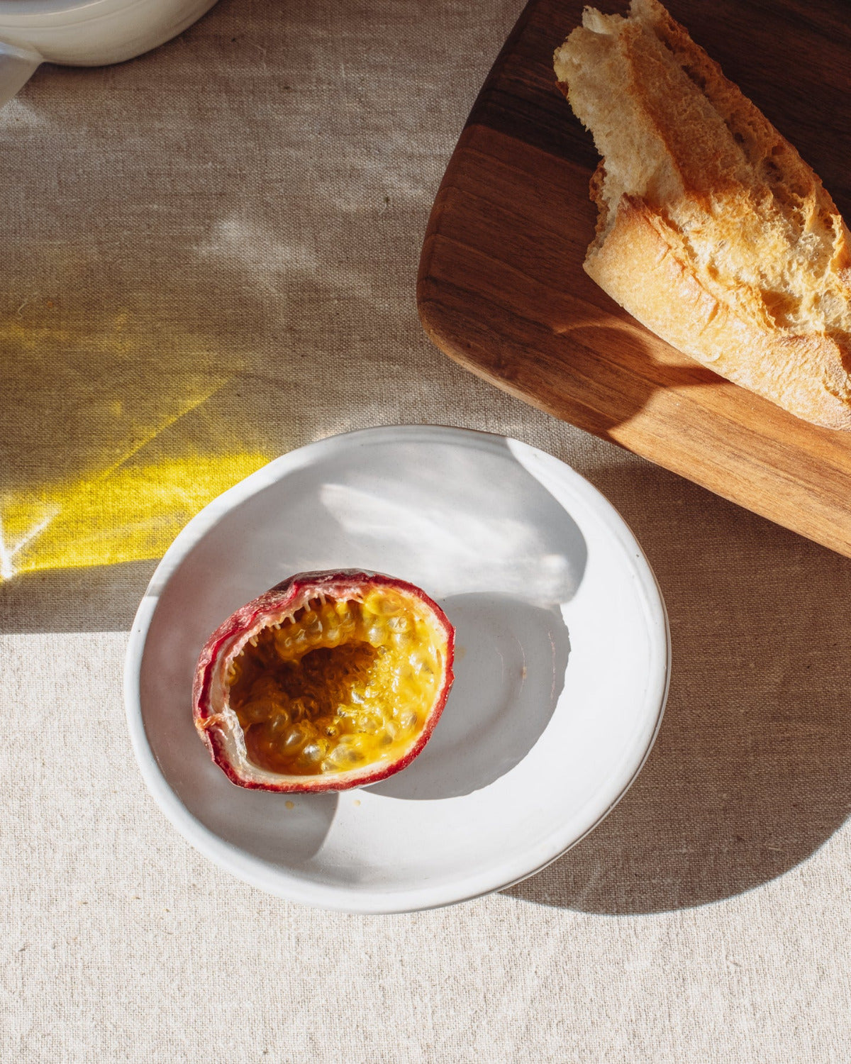 Passion fruit on a white oval bowl with bread on a wooden board in the background