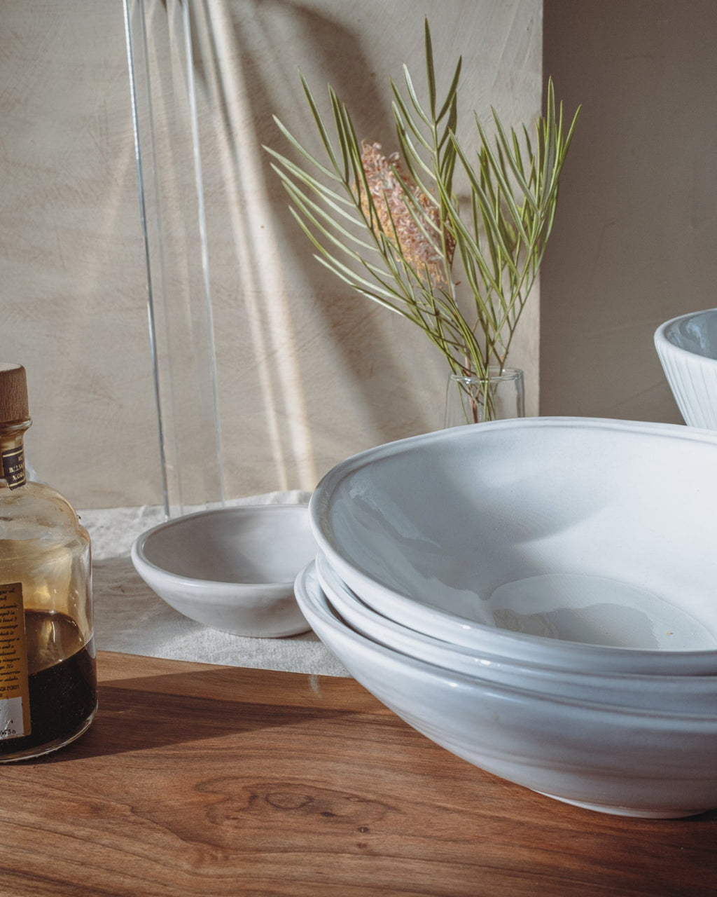 White ceramic bowls on a wooden surface with a plant and bottle in the background