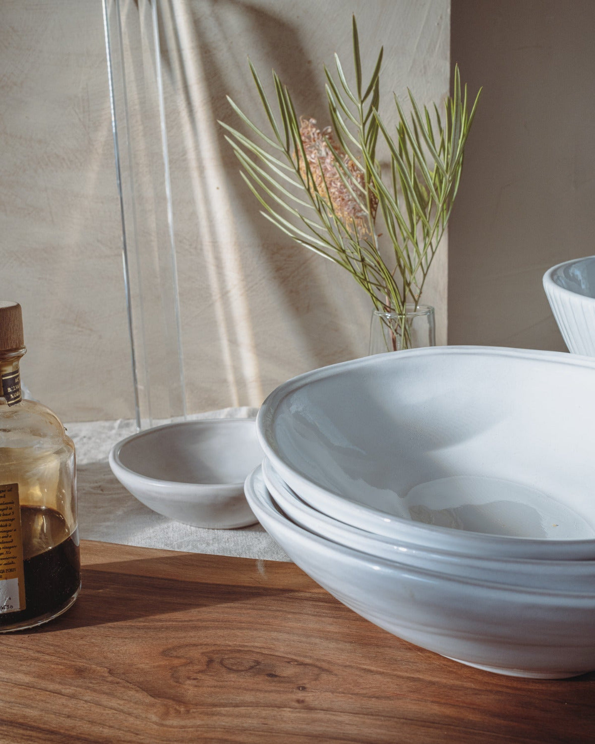 White ceramic bowls on a wooden surface with a plant and bottle in the background