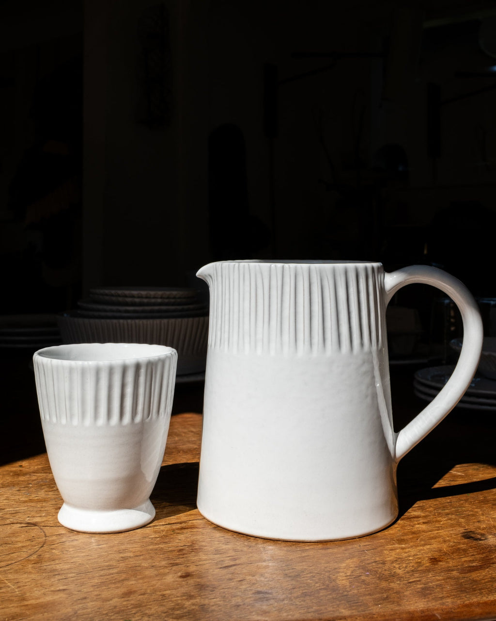 White ceramic pitcher and cup on a wooden surface with a dark background