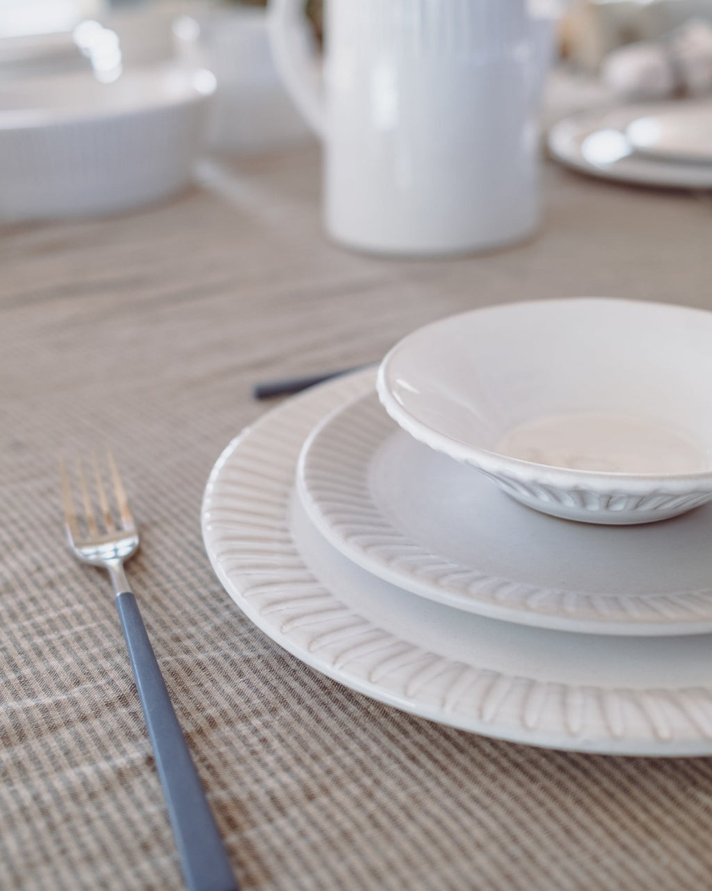 White ceramic plates stacked on a textured beige placemat with a fork.