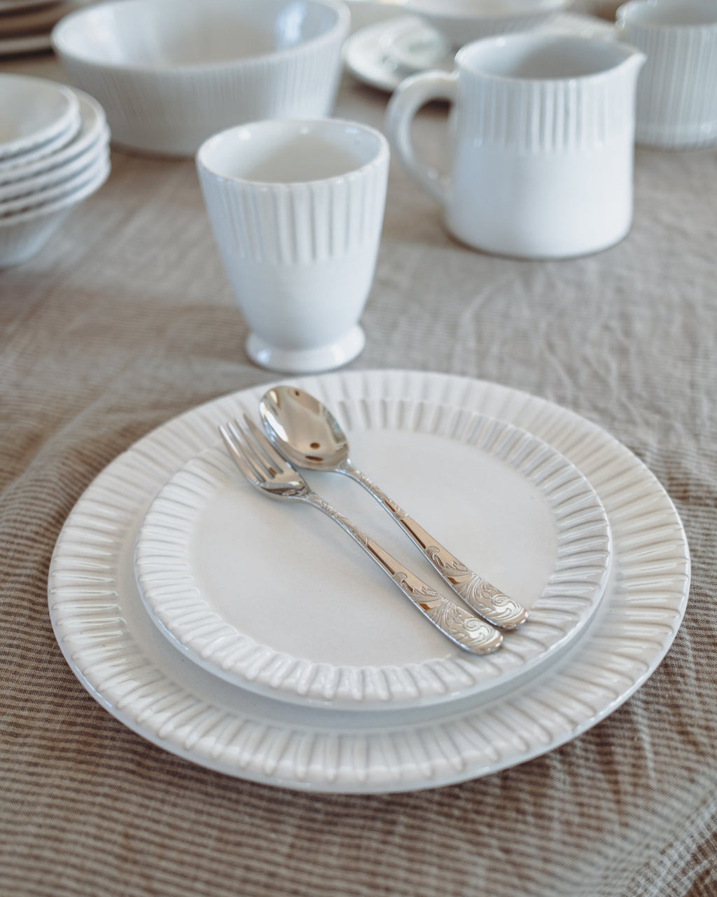 White ceramic tableware including plates, cups, and cutlery on a wooden surface.