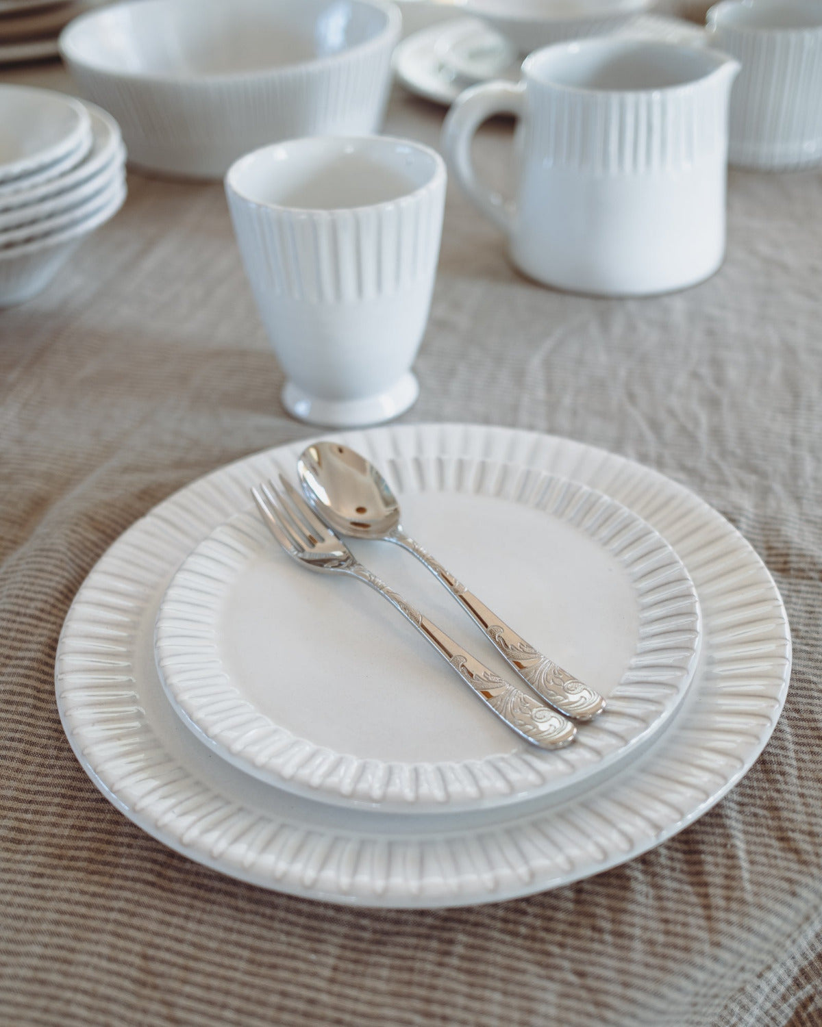 White ceramic tableware including plates, cups, and cutlery on a wooden surface.