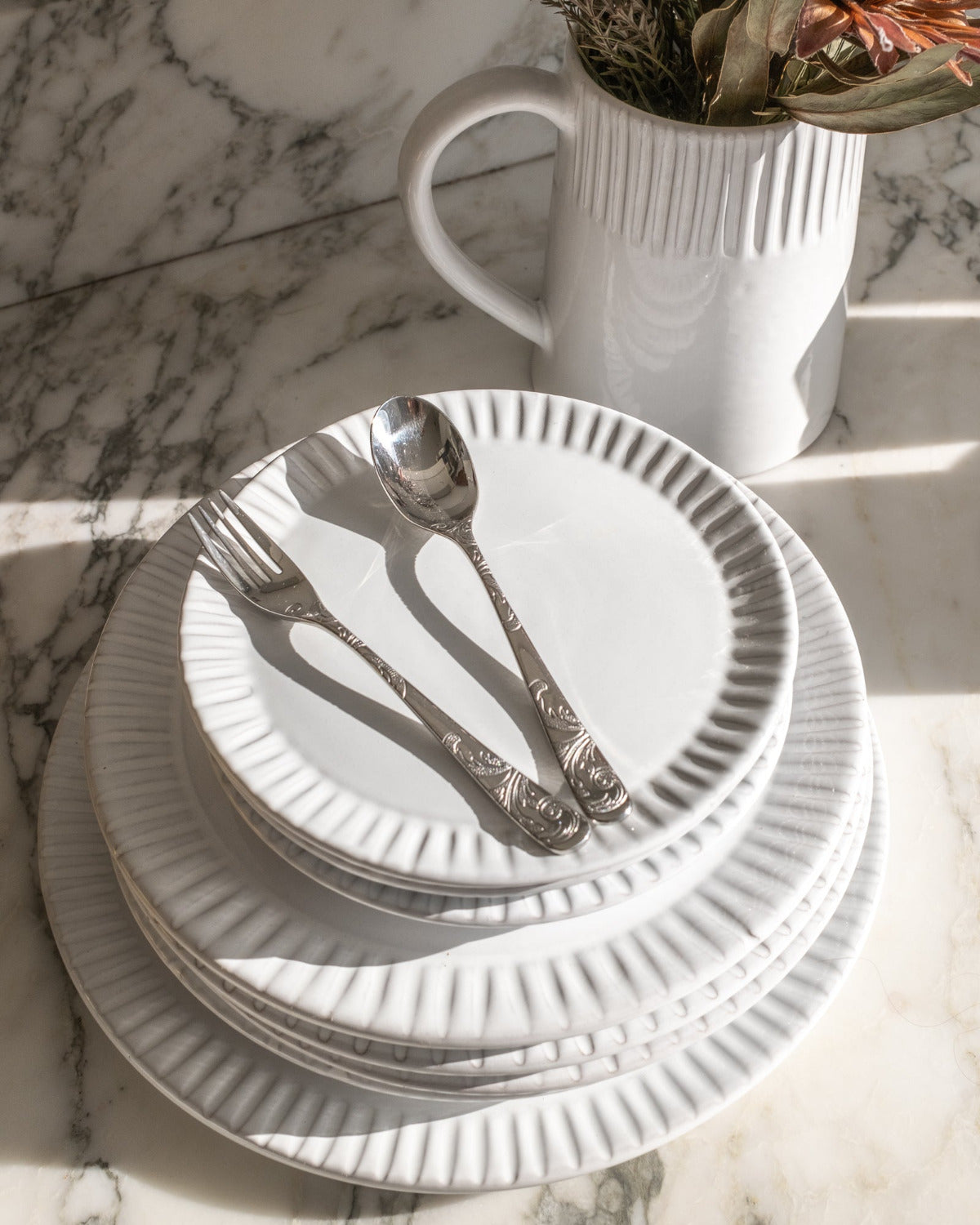 Stack of white plates with silverware on a marble surface