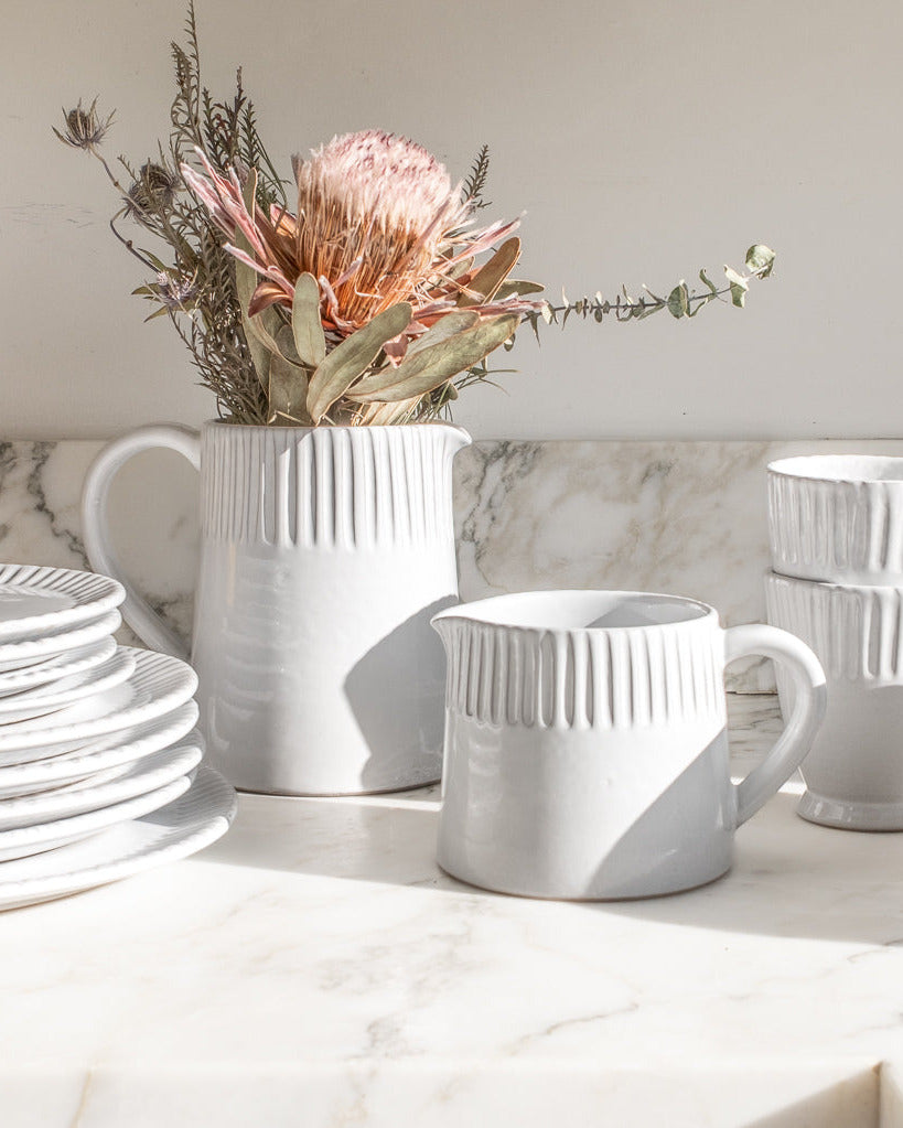 White ceramic tableware including plates, cups, and a pitcher on a marble surface.