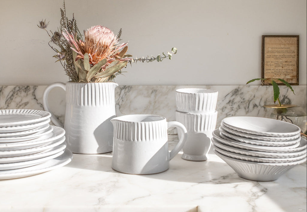 White ceramic tableware including plates, cups, and a pitcher on a marble surface.