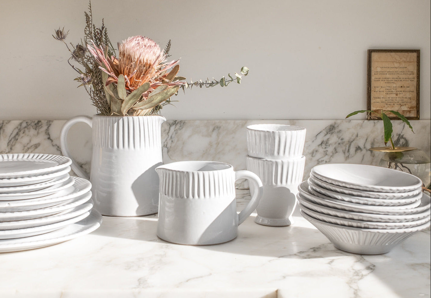 White ceramic tableware including plates, cups, and a pitcher on a marble surface.