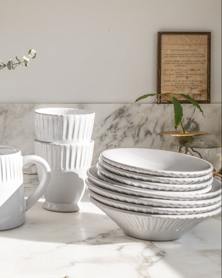 White ceramic tableware including plates, cups, and a pitcher on a marble surface.
