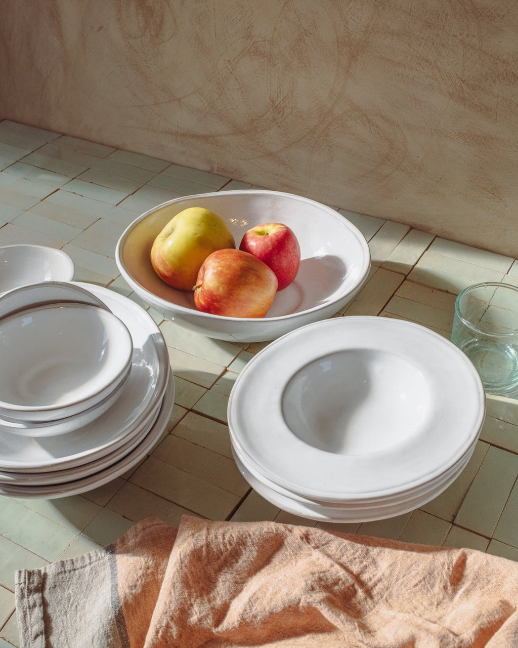 White ceramic plates and a bowl with fruits on a tiled floor.