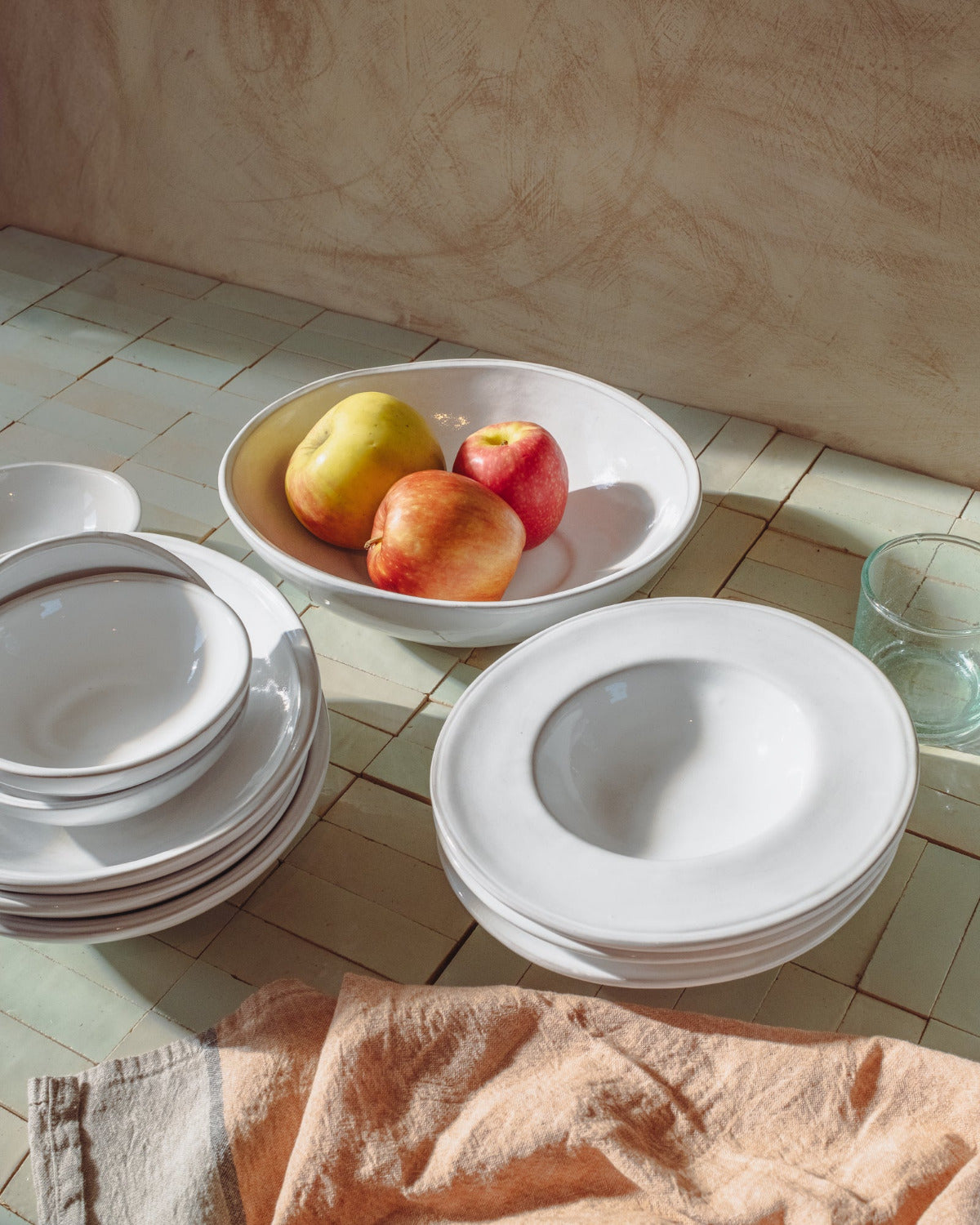 White ceramic plates and a bowl with fruits on a tiled floor.