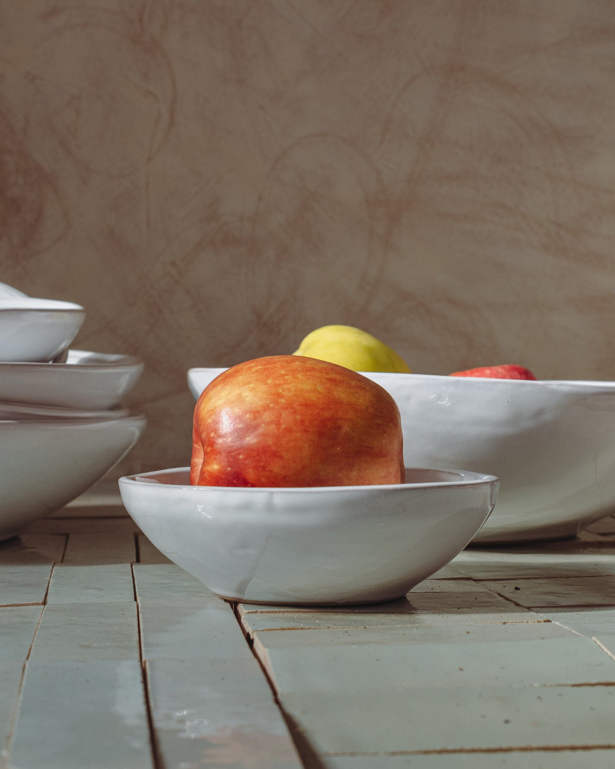 White small ceramic bowl with an apple on a zelige tile table