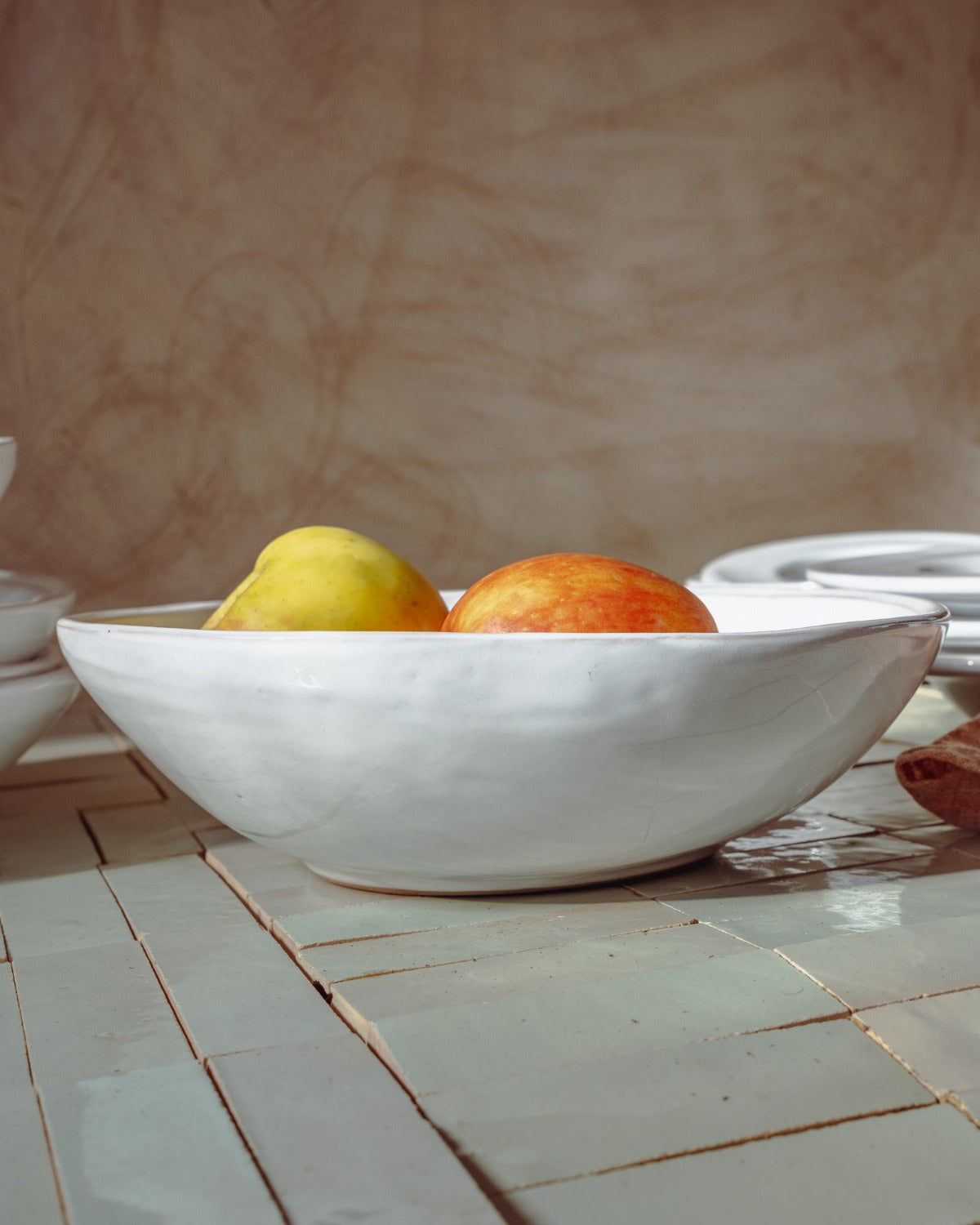 White ceramic bowl with a pear and an apple on a tiled surface