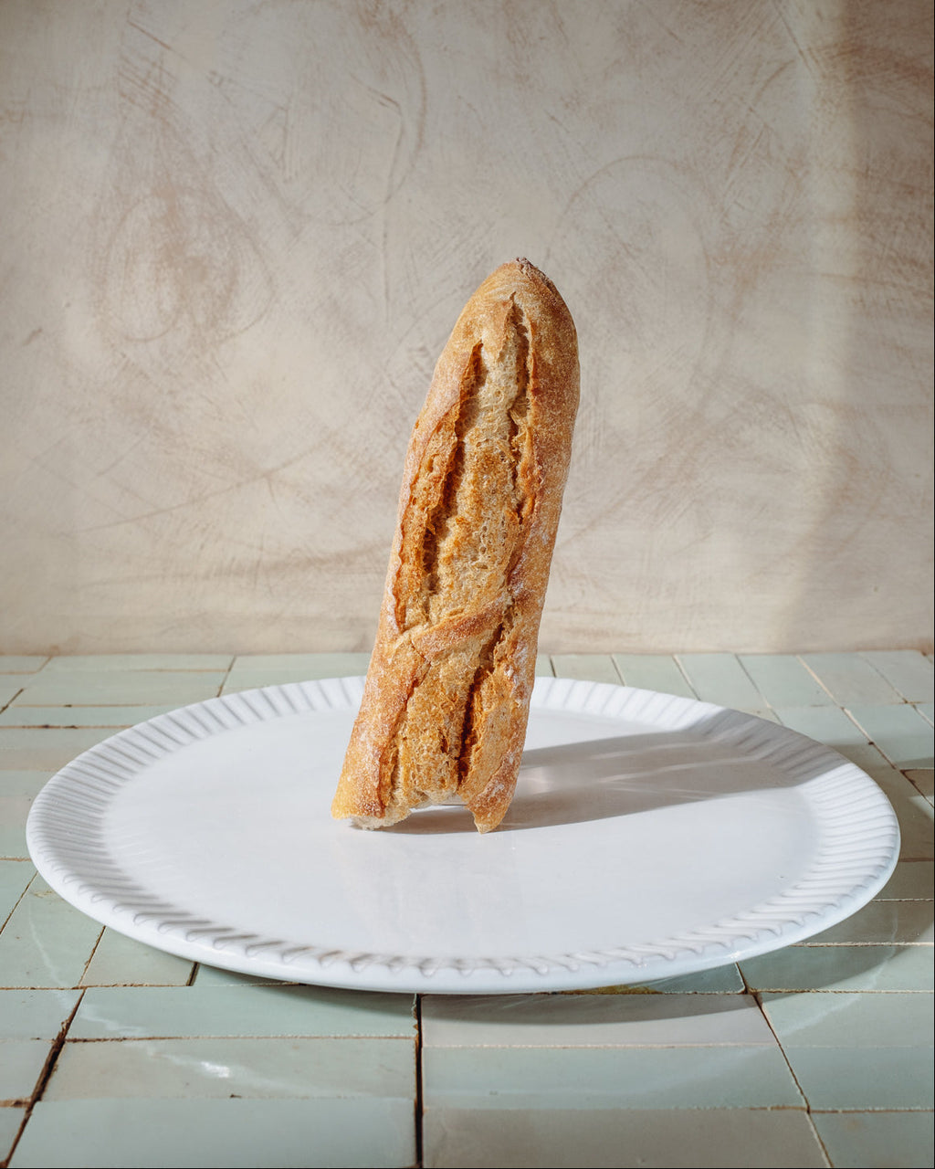 Baguette on a white serving platter with a lime wash background