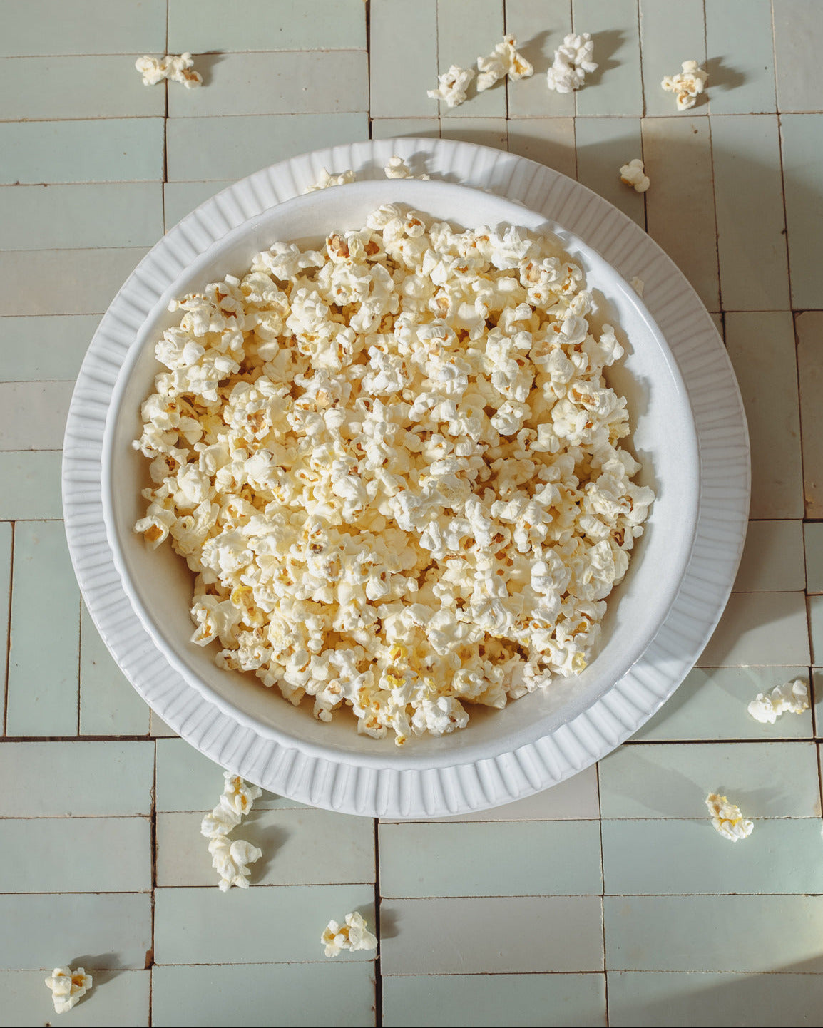 White ceramic plate with popcorn in a bowl on a tiled table.