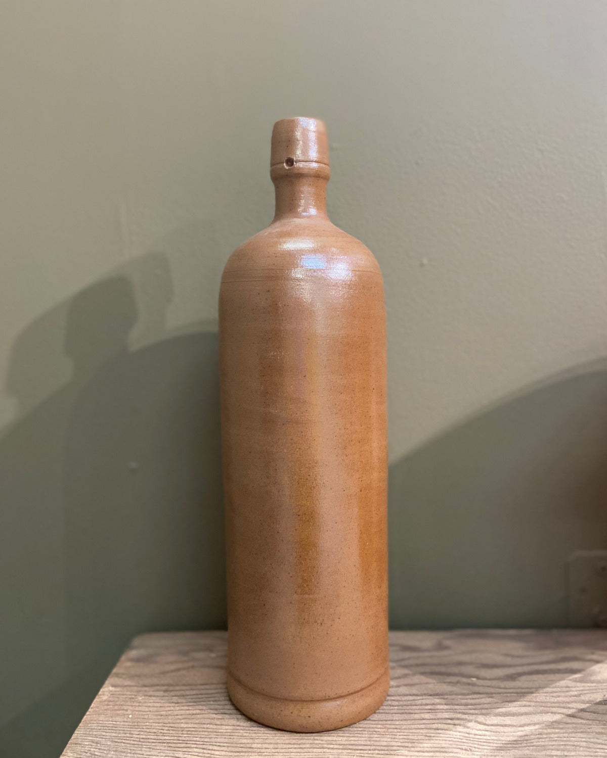 Brown ceramic bottle on a wooden surface with a plain background