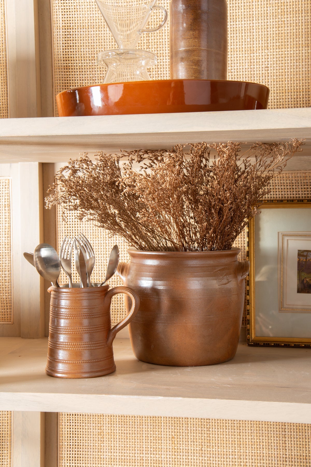 Decorative shelf with a brown ceramic jar, a smaller container with utensils, and a decorative vase.