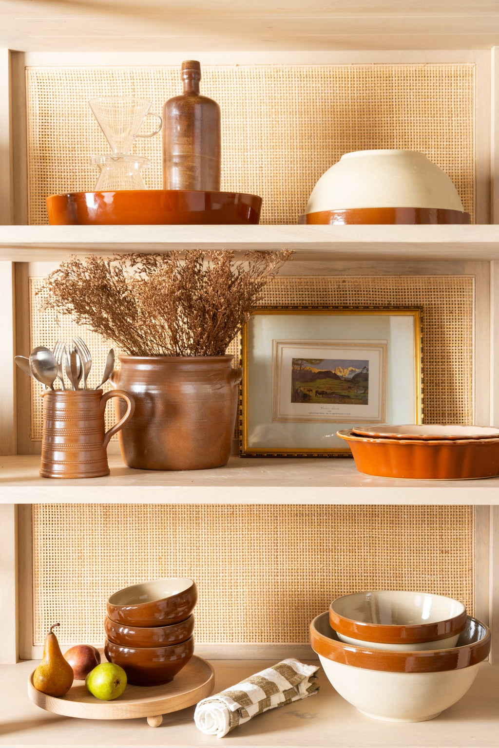 Decorative shelves with ceramic bowls, a pitcher, and a framed picture against a woven wall.