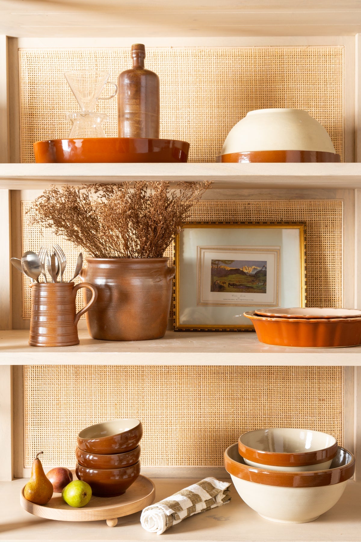 Decorative shelves with ceramic bowls, a pitcher, and a framed picture against a woven wall.