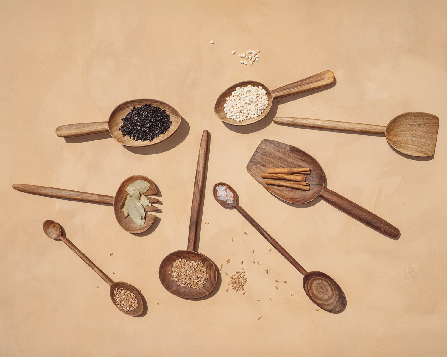 Wooden spoons with various spices and ingredients on a beige background